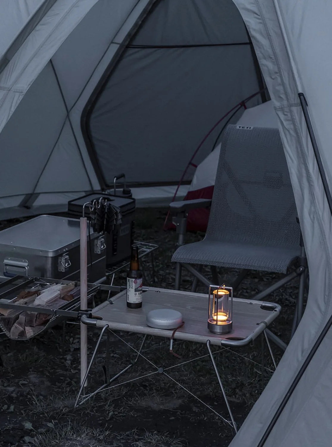 Camping scene with a tent, chair, and small table with a bottle and broadcrate crystal lantern inside.